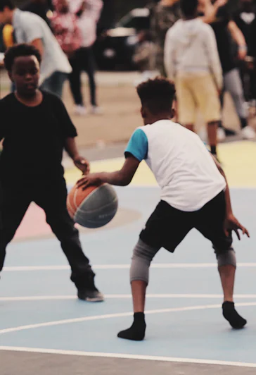 boy dribbling, bouncing a basketball with another boy defending