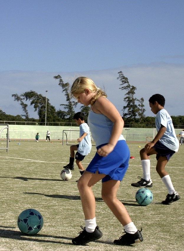 girl with soccer ball slightly in front of her as she moves to dribble it, boy with soccer ball on the outside of his foot to dribble it