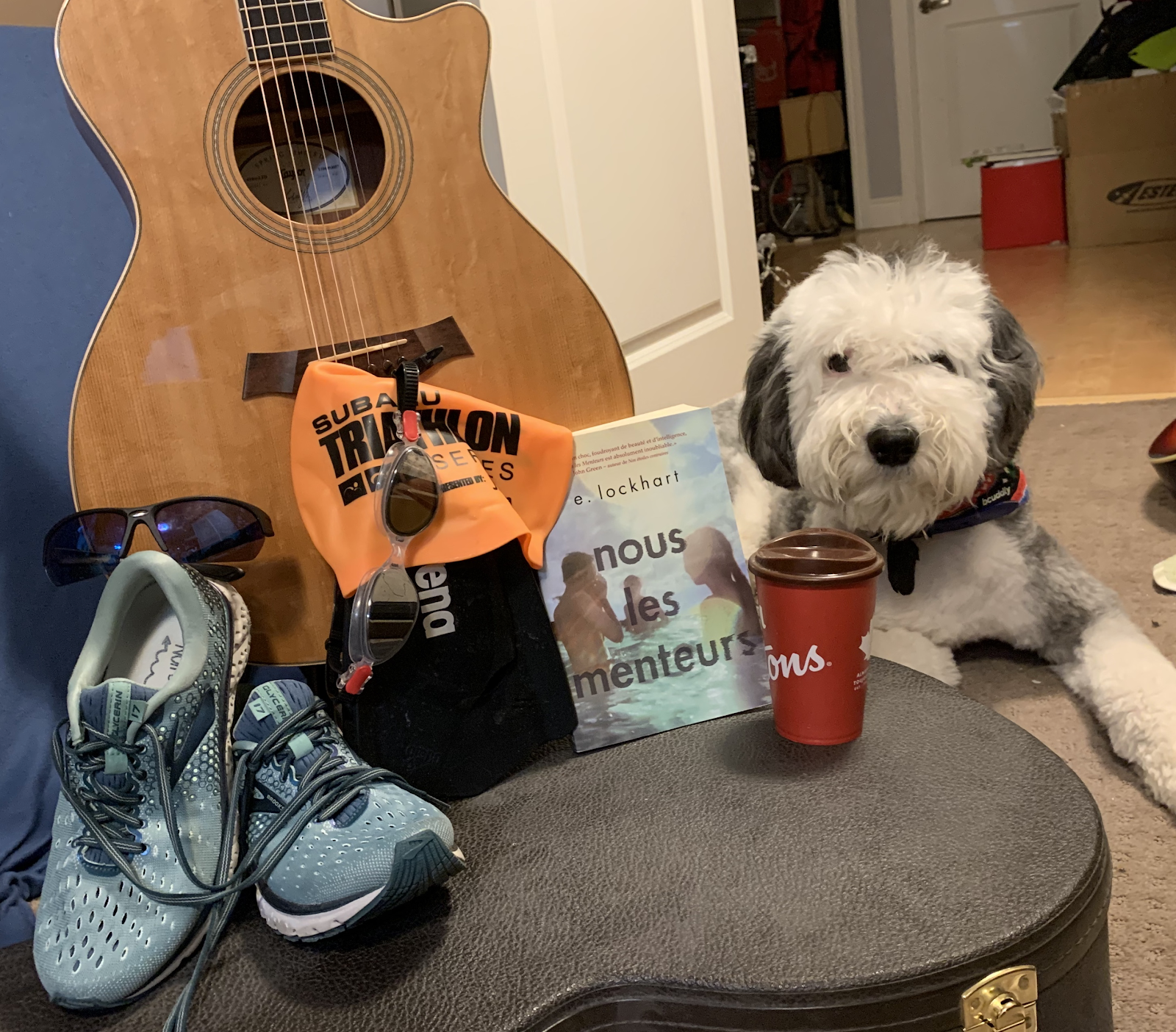 A collection of items, including running shoes, a guitar, a book, a cup of coffee and a dog.