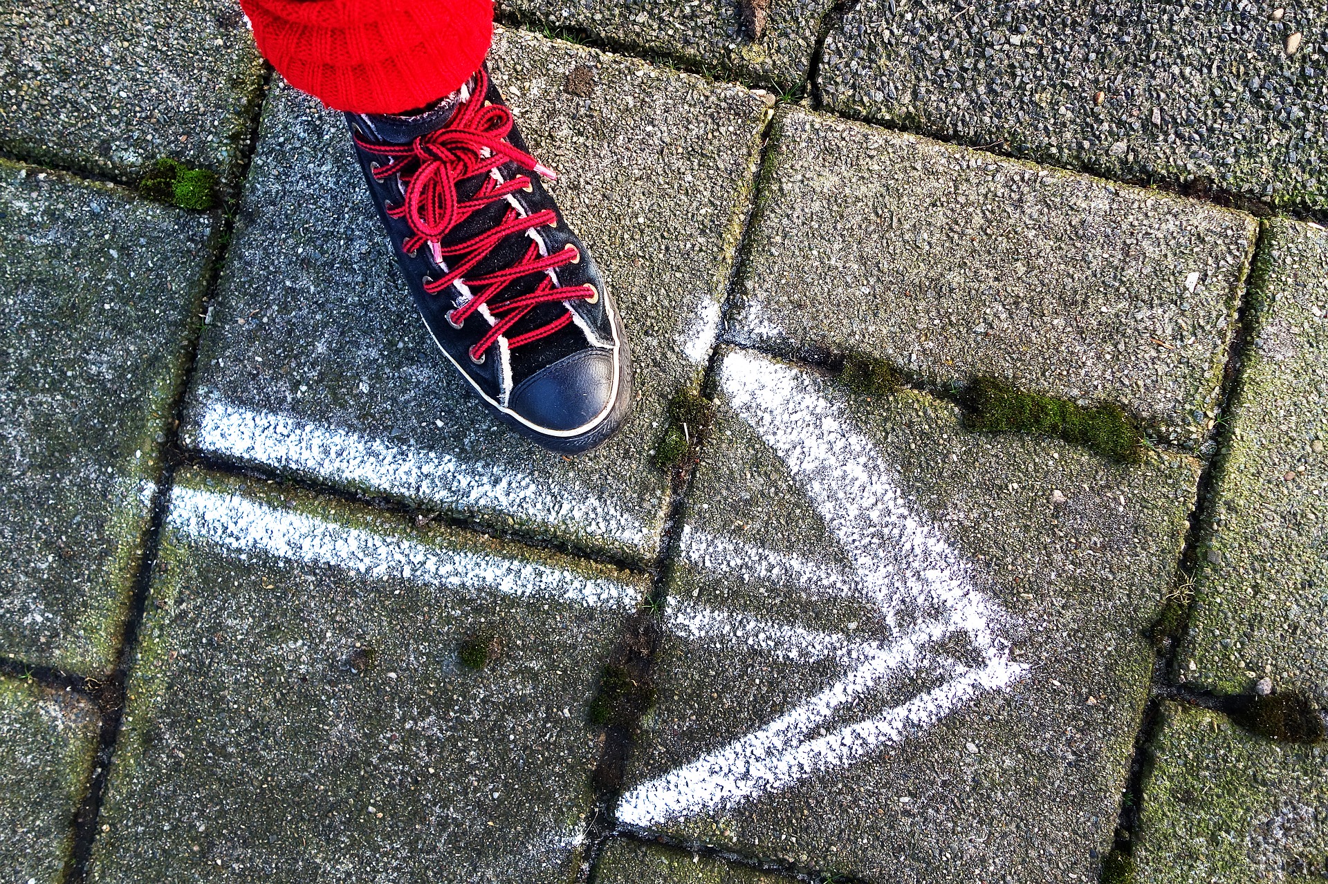 A foot wearing a black shoe, stepping beside a white arrow drawn with chalk on cement stones.