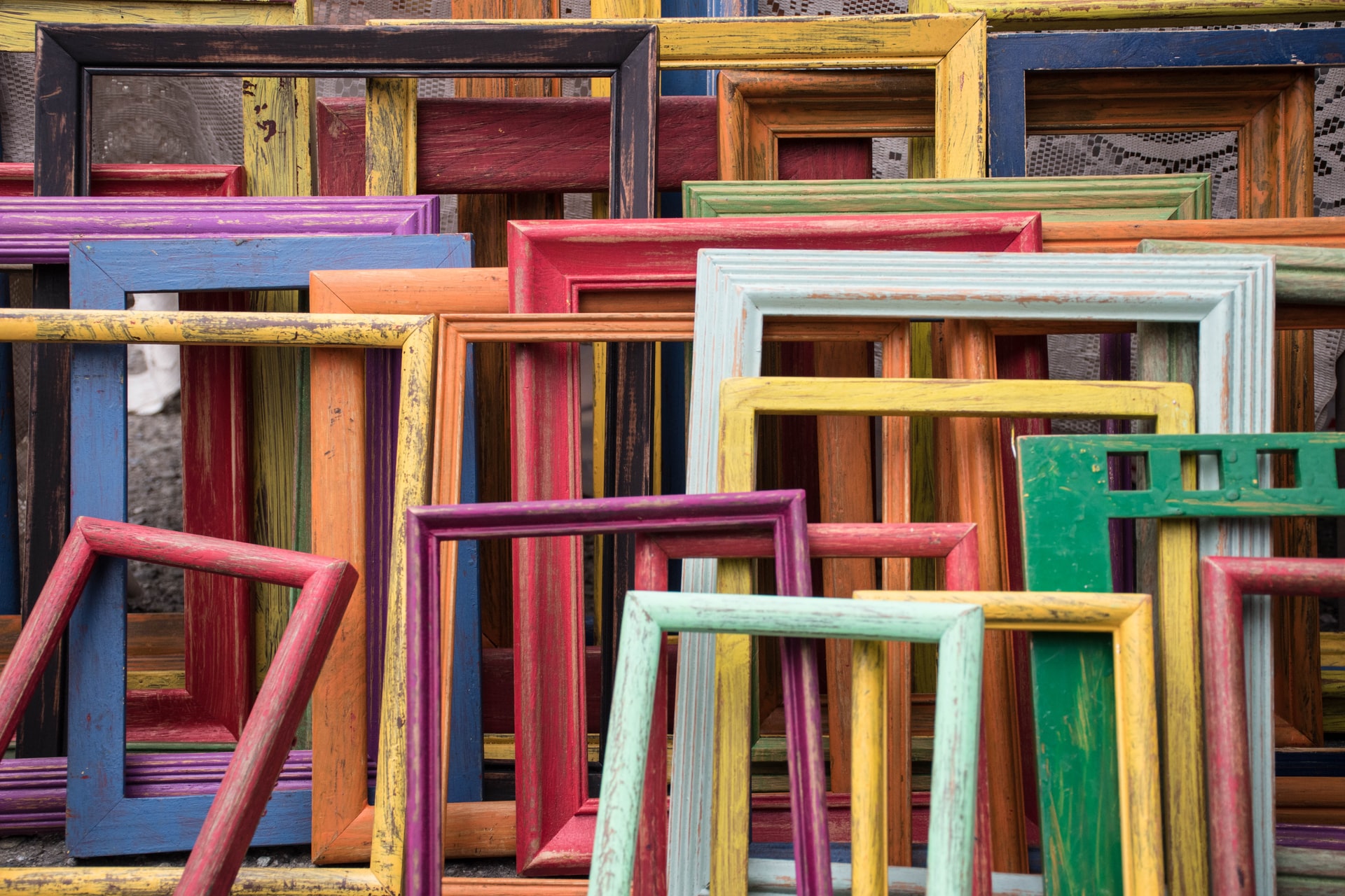 Picture frames of different colours and sizes leaning against a wall