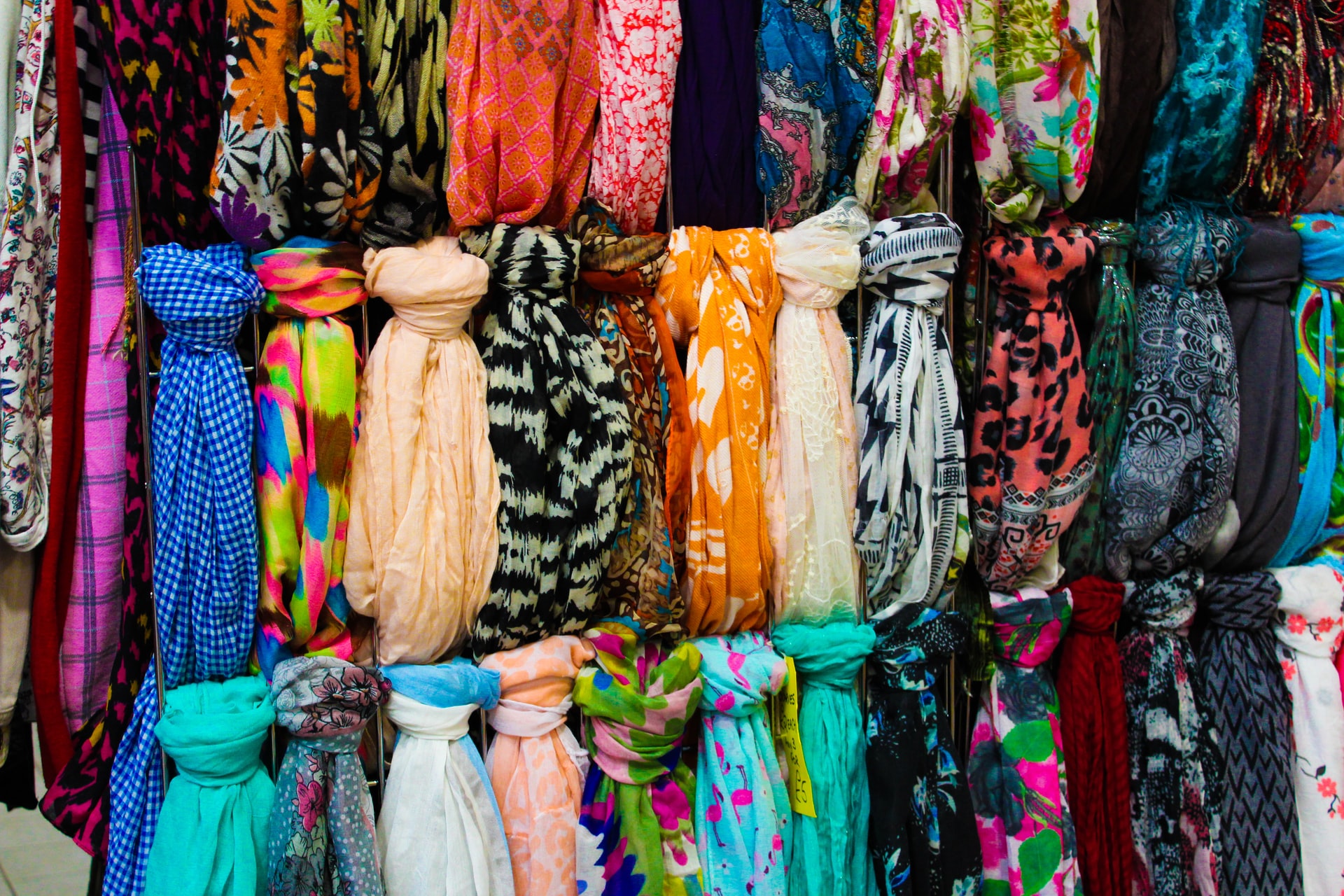 A display of a variety of multi-coloured scarves, tied in a knot across three bars and hanging down.