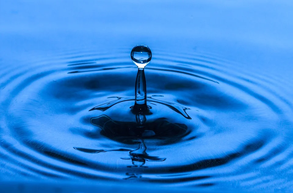 A water droplet creating a splash and ripple on the surface of blue water