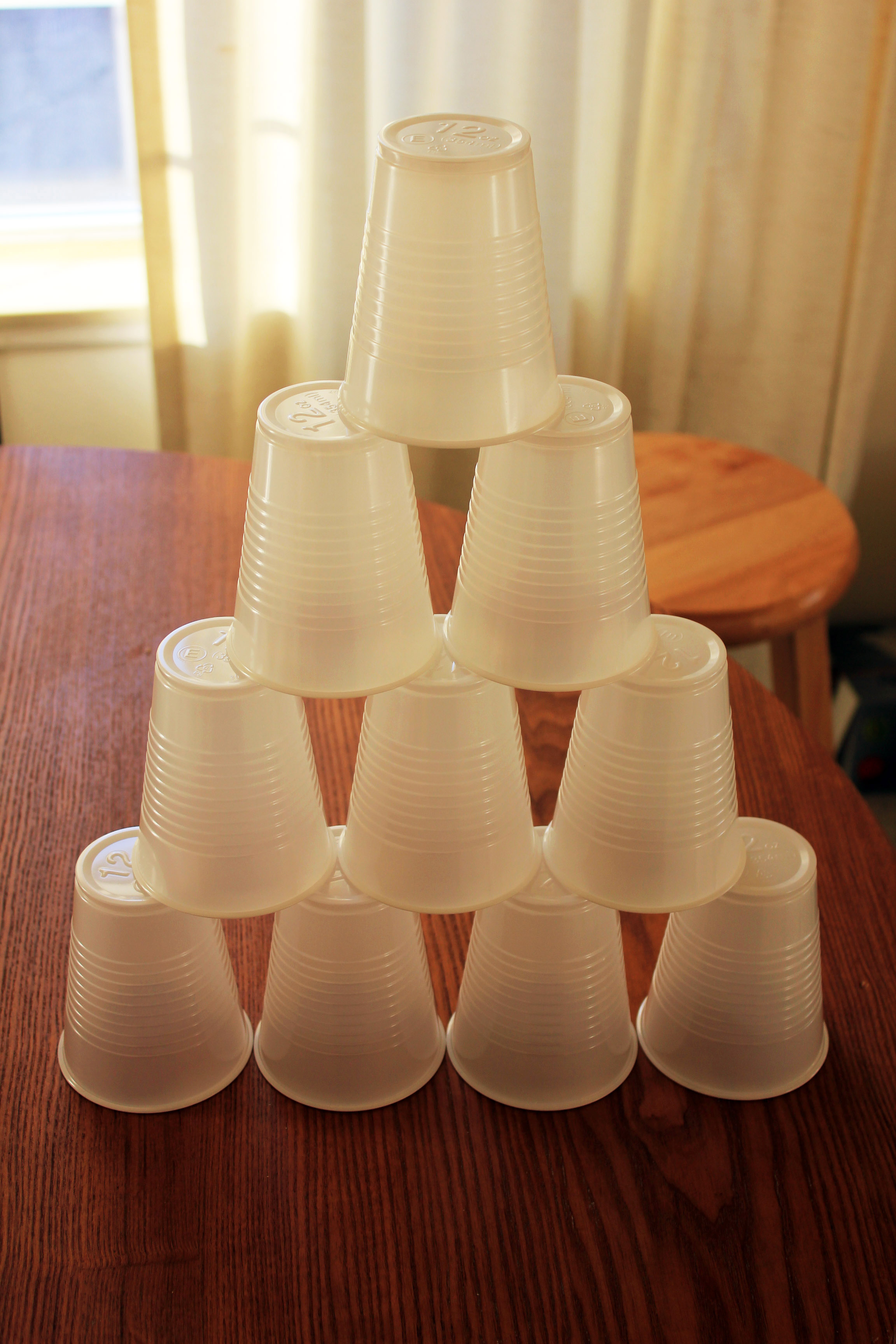 ten, clear plastic cups stacked, with four cups on the bottom, threes cups stacked on top of those, then two cups on top of the three, finally one cup on the very top