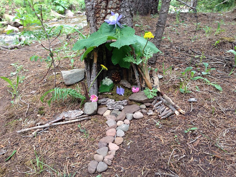A small fairy house built out of natural objects such as sticks, leaves, flowers, and bark.