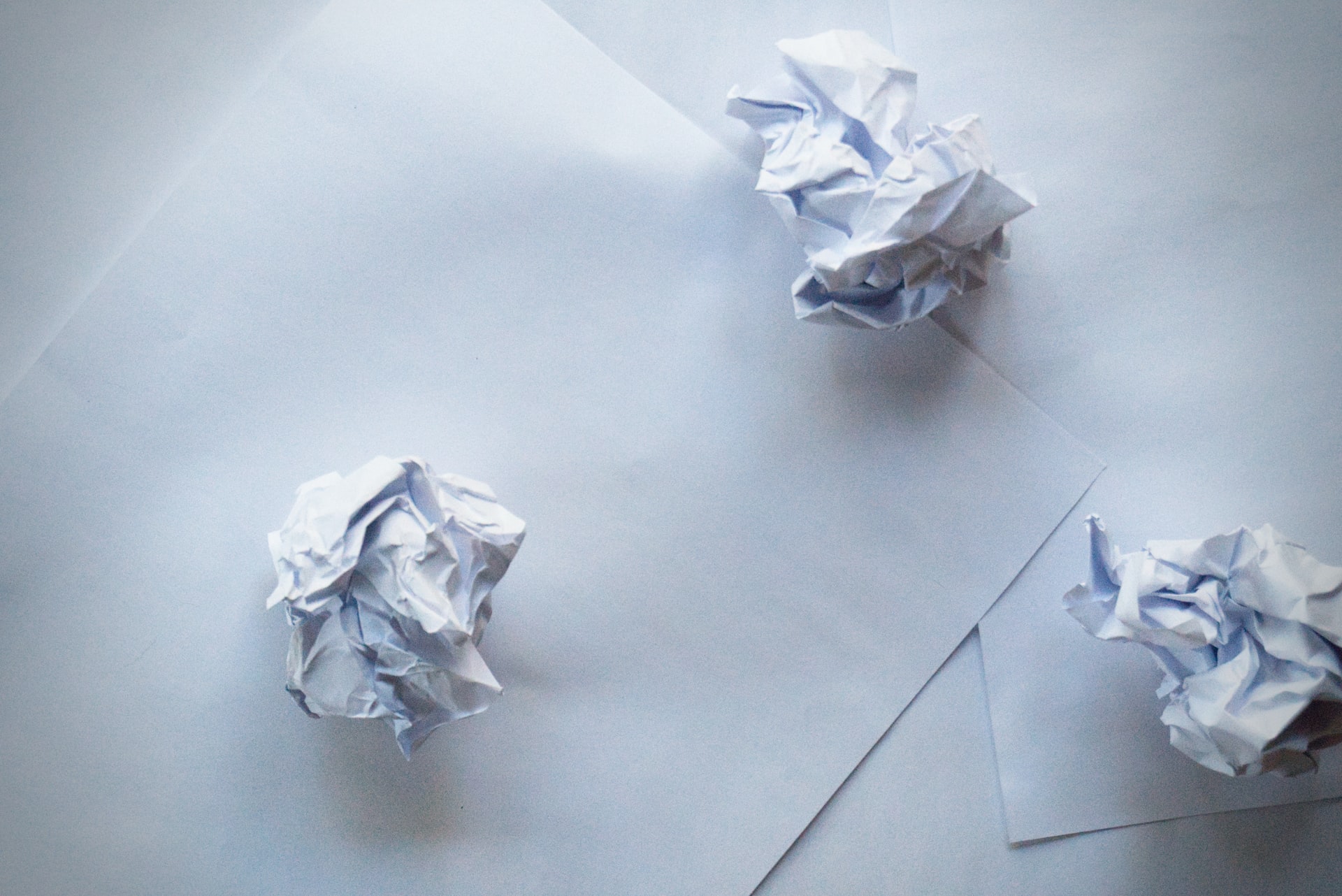 Three pieces of crumpled white paper balls sitting on top of two flat, pieces of white paper