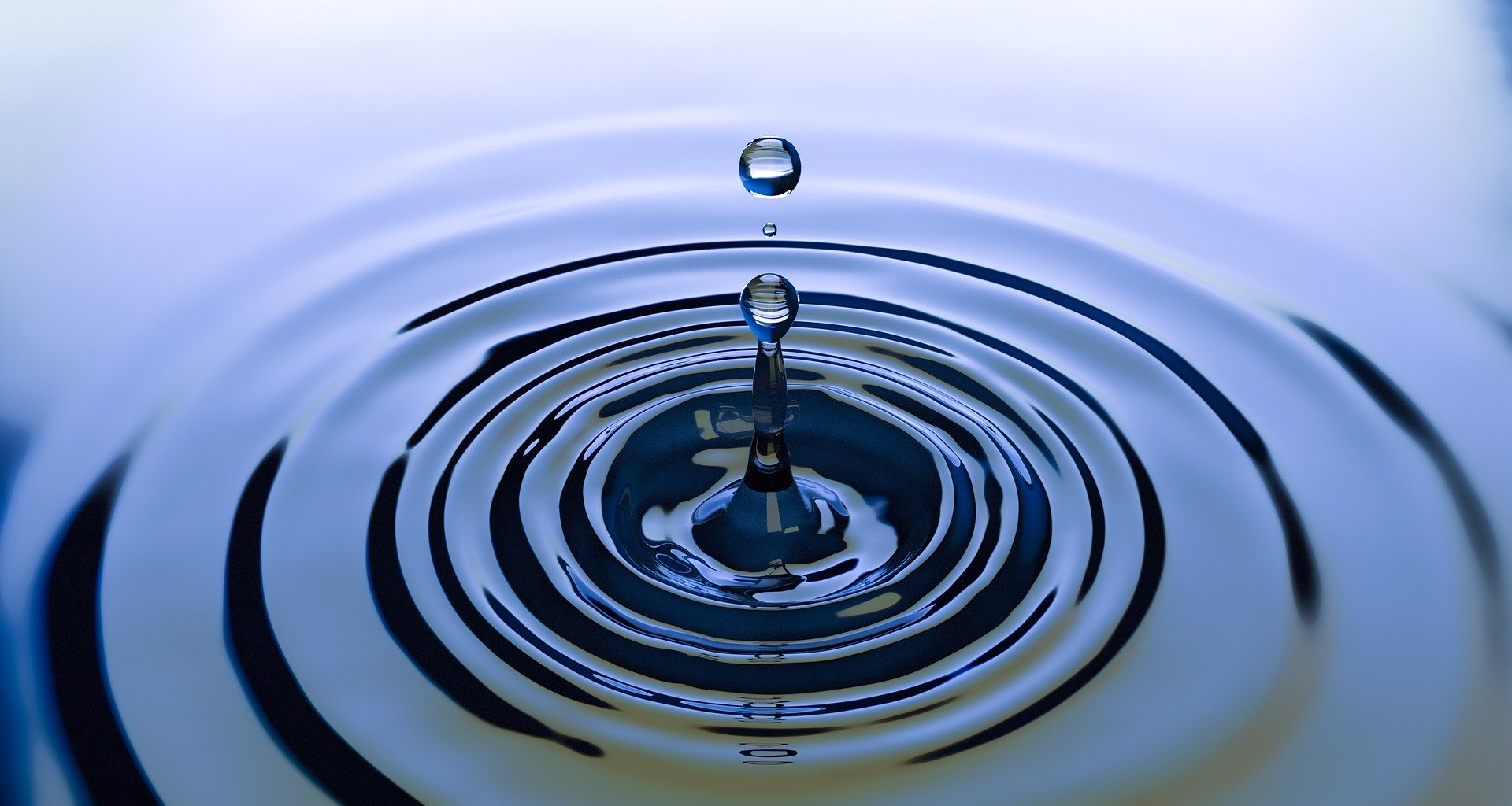 One drop of water above an expanding ripple on the surface of blue water.